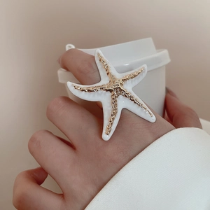 Macro shot of a white starfish ring with golden accents and detailed texture on finger