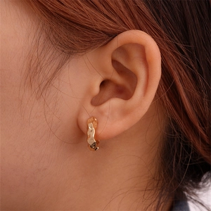 Close-up of golden metal ear cuff with hammered texture on female model's ear