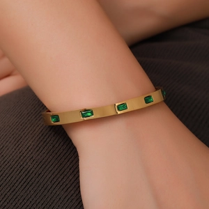Detailed close-up of a gold-plated titanium steel cuff featuring inlaid green emerald-cut stones