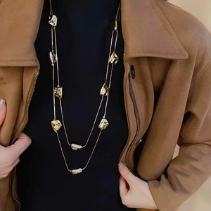 Dettaglio della collana geometrica dorata a due strati indossata su un maglione autunnale