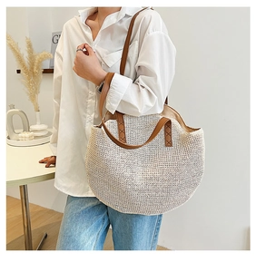 Detail of hand-woven straw tote bag showing brown leather straps and reinforced stitching