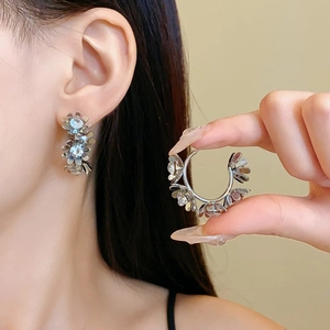 Close-up of sparkling silver flower stud earrings with crystals on a model's ear