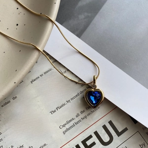 Macro shot of gold snake chain with heart-shaped blue zircon pendant on ceramic dish