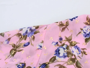 Dettaglio del tessuto in chiffon rosa con motivi floreali blu e accenti dorati sulla camicetta