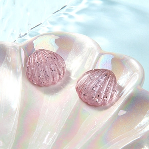 Close-up of pink glitter resin shell earrings in a holographic tray with water ripple effects
