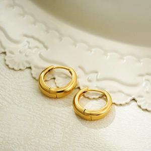 Close-up of polished 18K gold hoop earrings on a textured surface with soft lighting