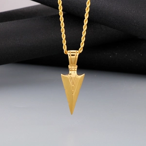 Detail of a golden arrow pendant with linear patterns on a gold rope chain necklace