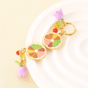 Detail of golden enamel lemon slice and flower drop earrings on a white tray