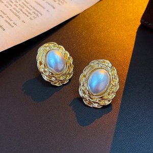 Detail view of vintage gold-rimmed oval pearl earrings on elegant textured background