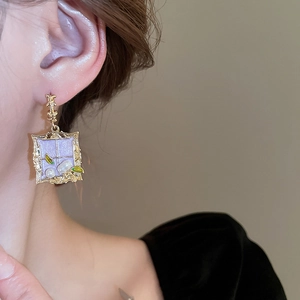 Close-up of vintage square pearl drop earring with purple inlay and green leaf detail
