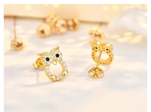Detailed macro view of gold-plated owl earrings with sparkling white and black zircon stones