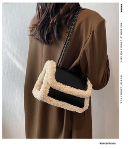Detail of a chic black shoulder bag with white faux shearling trim on a brown wool coat
