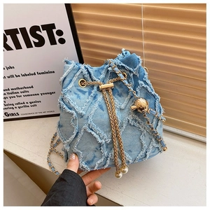 Detail of blue denim bucket bag featuring golden chain strap and pearl fringe accents