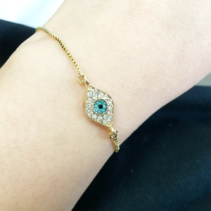 Detailed close-up of golden evil eye bracelet with blue and white rhinestones on wrist