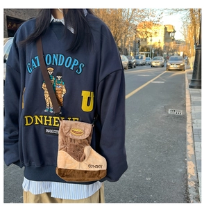 Detail of a brown plush boot-shaped crossbody bag worn with a navy cartoon sweatshirt