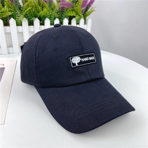 Detail of navy cotton baseball cap featuring a black 'Hand Made' woven patch with tree icon