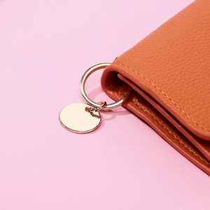 Close-up of brown litchi grain leather wallet featuring gold metal ring and round tag charm