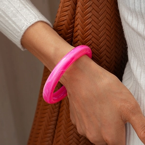 Detail of pink acrylic bangle with marble texture worn on model wrist over knitwear