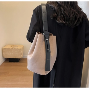 Detailed side view of khaki matte leather bucket bag with black strap on model