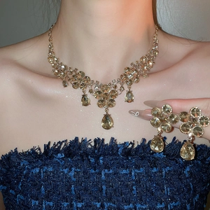 Close-up of luxury gold necklace and drop earrings set with champagne crystals on a model