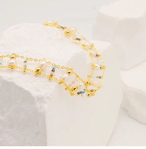Detailed close-up of gold chain necklace with white pearls and colorful beads on stones
