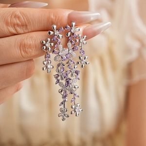 Close-up of sparkling flower and butterfly tassel earrings with purple zircons