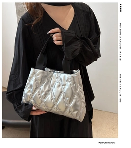 Detail of silver quilted tote bag with metallic finish and black woven strap handles