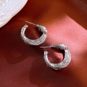 Close-up of silver knot earrings on red silk background with detailed twisted texture