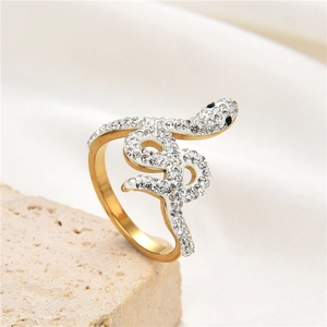 Golden snake ring with crystals and green stone eyes on a beige stone surface
