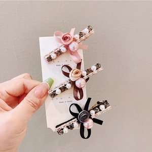 Detail of three crystal and pearl hair clips with ribbon flowers on display card