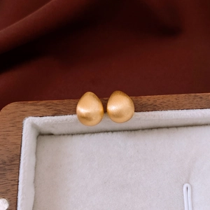 Macro detail of teardrop gold plated earrings with a brushed matte finish on wood