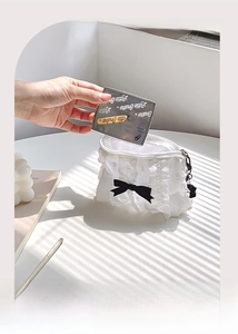 Dettaglio del beauty case in pizzo bianco con fiocco nero e ciondolo di perle sulla zip