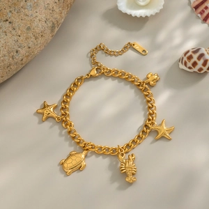 Bracciale in acciaio dorato con ciondoli stella marina e tartaruga su sfondo spiaggia