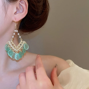 Close-up of shell pearl tassel earrings with light green leaf pendants on a female model