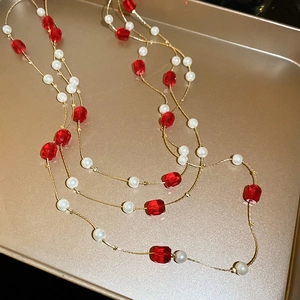Detail of layered gold necklace with red faceted crystals and white pearls on a tray