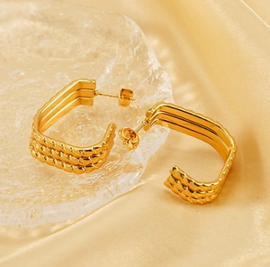 Detailed macro view of gold-plated multi-layer twisted rope earrings on a glass tray