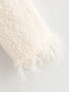 Close-up of cream knit fabric texture with frayed fringe detail on the sleeve cuff