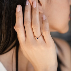 Close-up of rose gold V-shaped ring featuring a round blue December birthstone