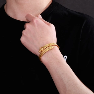 Detail of man wearing a gold twisted wolf head bracelet against a black background