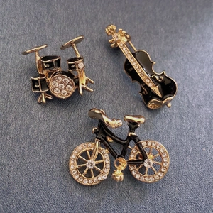 Detailed view of rhinestone-studded drum, violin, and bicycle brooches on blue fabric