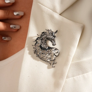 Macro detail of a vintage horse brooch with hollow metalwork and diamonds on white lapel