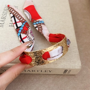 Detailed close-up of a gold hammered cuff bracelet with a woven silk scarf accent