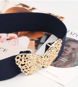 Detail of a large golden butterfly buckle on a navy blue elastic waist belt for dresses