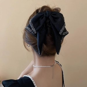 Detail view of large black bow hair claw clip with sparkly rhinestone trim on woman's hair