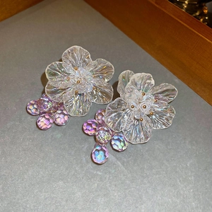 Close-up of iridescent acrylic flower earrings with purple beaded tassels and gold stamen