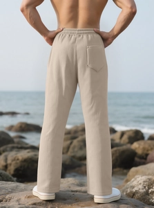 Rear view of men's beige straight pants with vertical textures on a seaside rocky coast