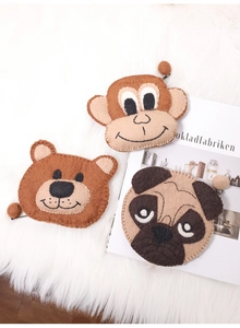 Flat lay of monkey, brown bear, and pug felt coin purses on a soft white rug