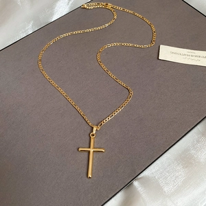Macro shot of 18k gold plated cross pendant and Figaro chain on textured gray card