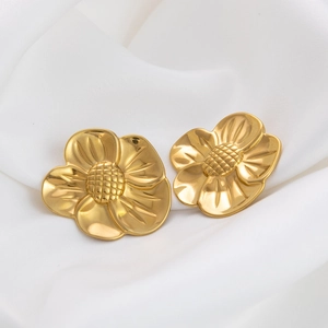 Macro detail of gold-plated flower earrings on white silk fabric with soft shadows