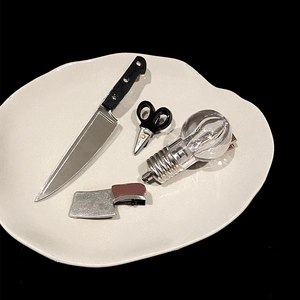 Detailed set of creative mini knife and lightbulb hairpins on a white ceramic plate